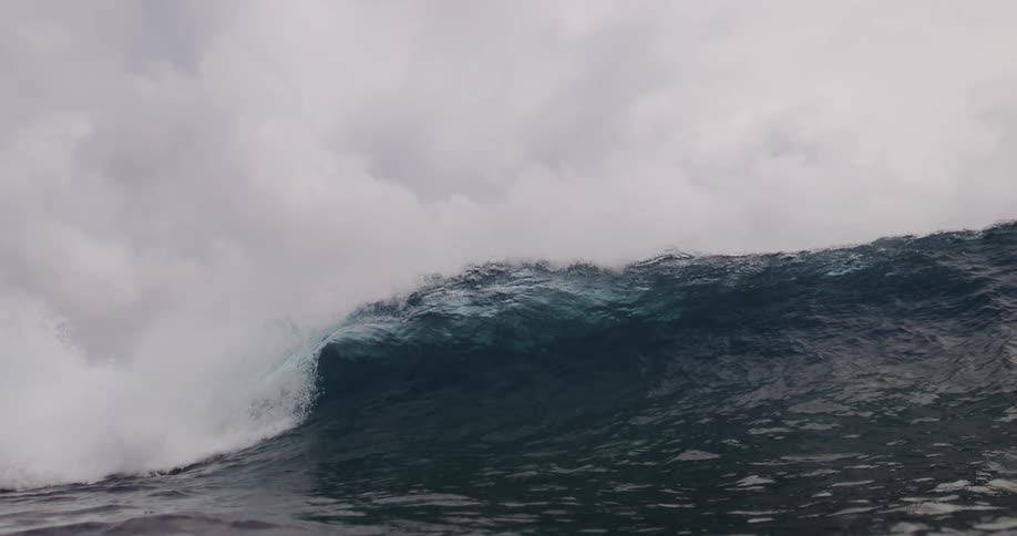 A powerful ocean wave is breaking and churning white water under a heavy overcast sky