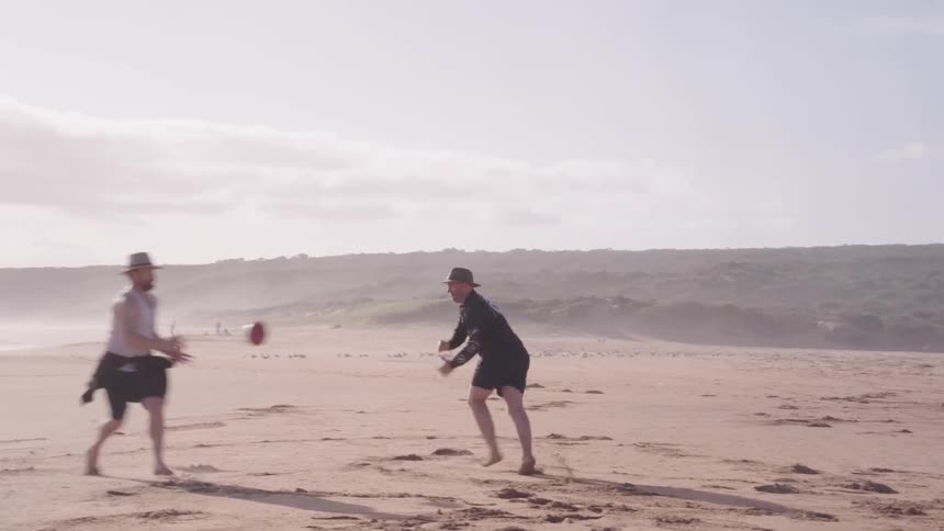 Friend tossing and punting a football to each other having fun on the beach