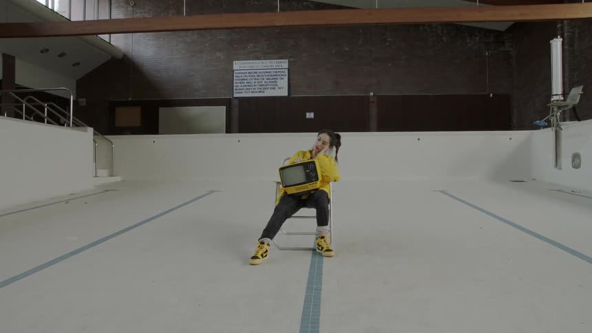 Woman sits on a chair in an empty pool with a tv on her lap