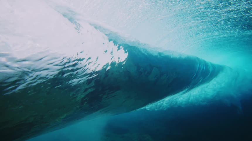 An underwater of the smooth dark underside of a wave as it moves above creating a contrast with the lighter turbulent water near the surface and the deeper blue below
