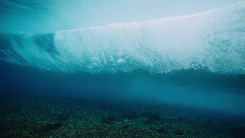 From an underwater perspective near the seabed a large wave creates turbulent whitewater across the surface as it passes overhead