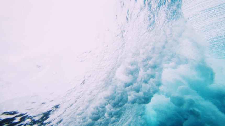 View from below the water and a wave passing with force and foam