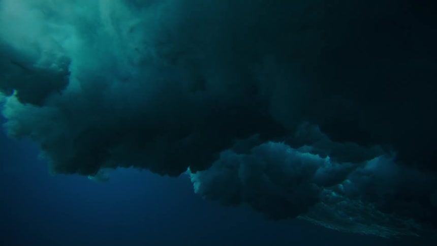 Underwater view of the ocean with foam rising on the surface of a wave