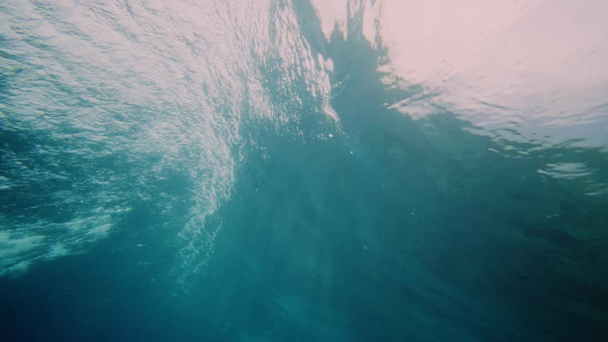 An underwater view of sunlight filtering through the surface creating bright patches and shadows in the clear turquoise water that fades into a deeper blue below