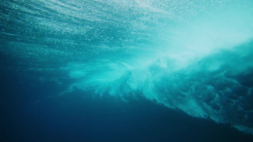 Underwater view of a turquoise blue ocean and a crashing wave