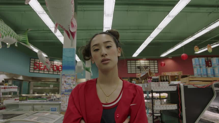 Woman looking stoically into the camera while she stands in a grocery store