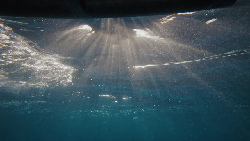 Sunlight streams through the surface of the water creating bright rays that penetrate the clear blue depths