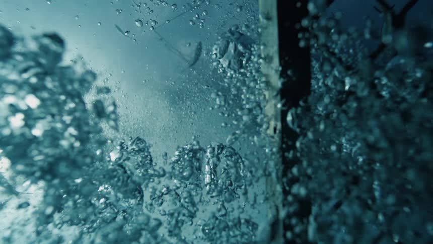 Looking up from inside a submerged cage small fish swim through sunlit water as bubbles rise