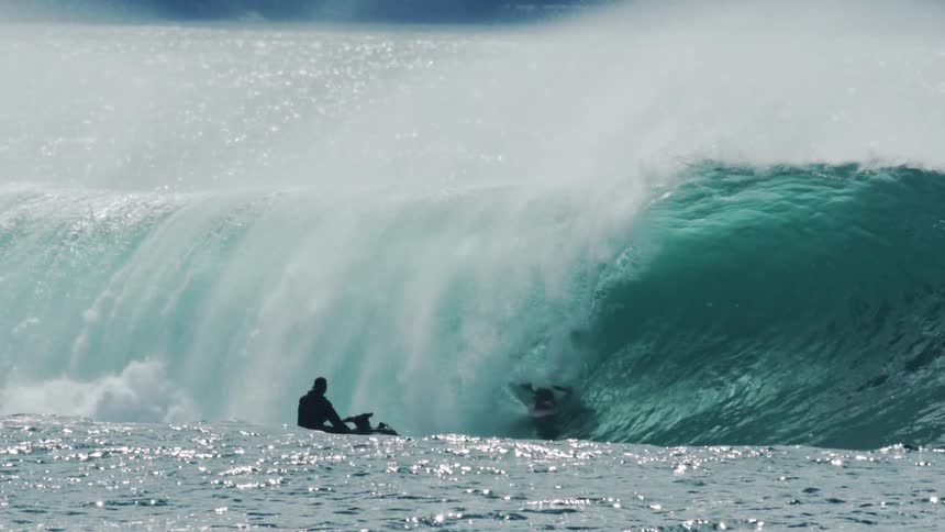 In slow motion a surfer rides deep inside the barrel of a large breaking wave on a sparkling sunlit ocean