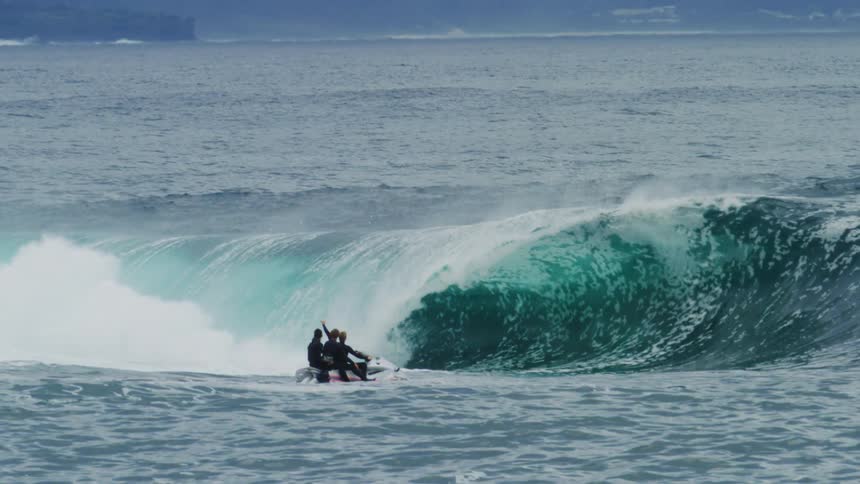 Three people on a jet ski in the ocean with a tubular wave occurring in the background