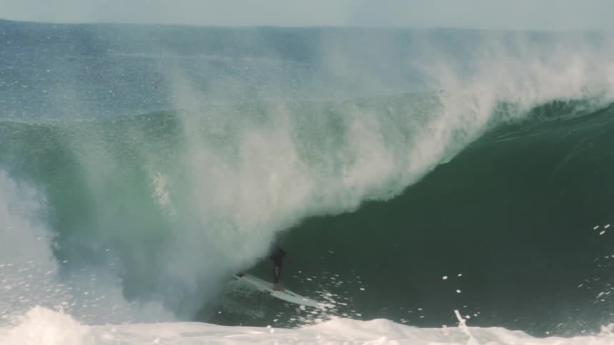 A surfer skillfully maneuvers their board deep inside the hollow barrel formed by a large powerful ocean wave just as it starts to crash and enclose them