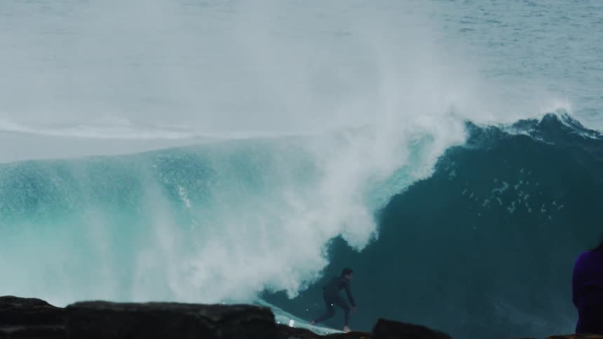 People on the shore watch a surfer and jet skiers enjoying the water