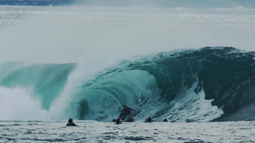 Several surfers in an ocean with one of them surfing a tubular wave