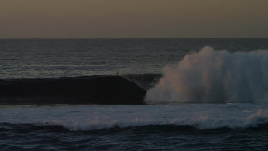 Surfers and a person on a jet ski in an ocean at dawn with strong waves