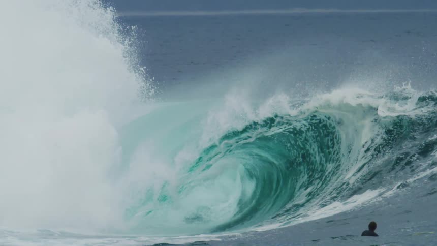 People in the sea enjoy a large turquoise blue tubular wave breaking upon impact