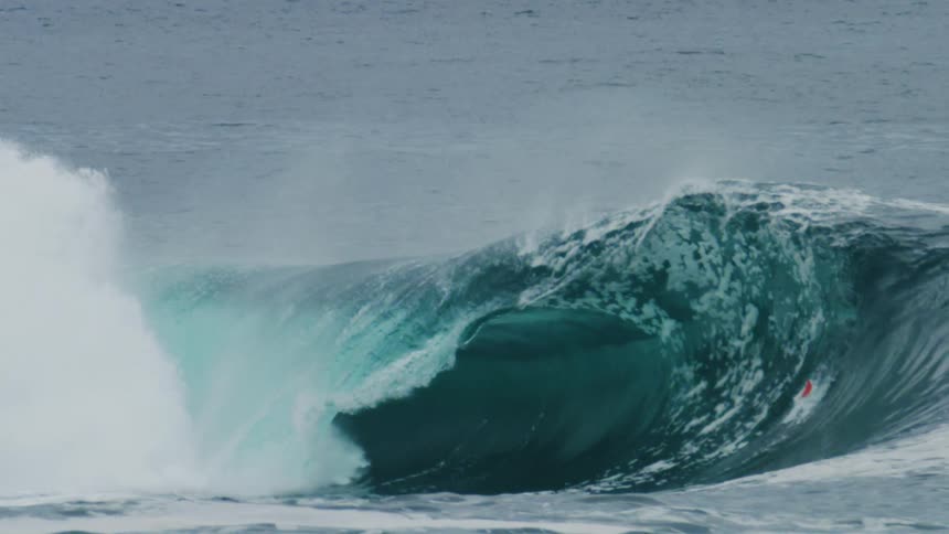Person wearing flippers dives into the water near a breaking wave during the daytime