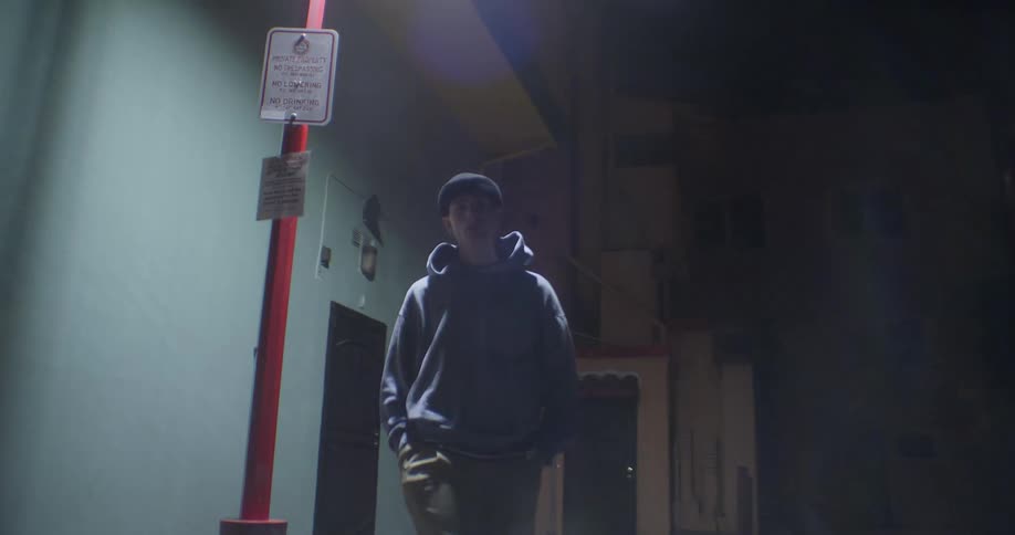 Young man in an alley at night leaning against a lamppost