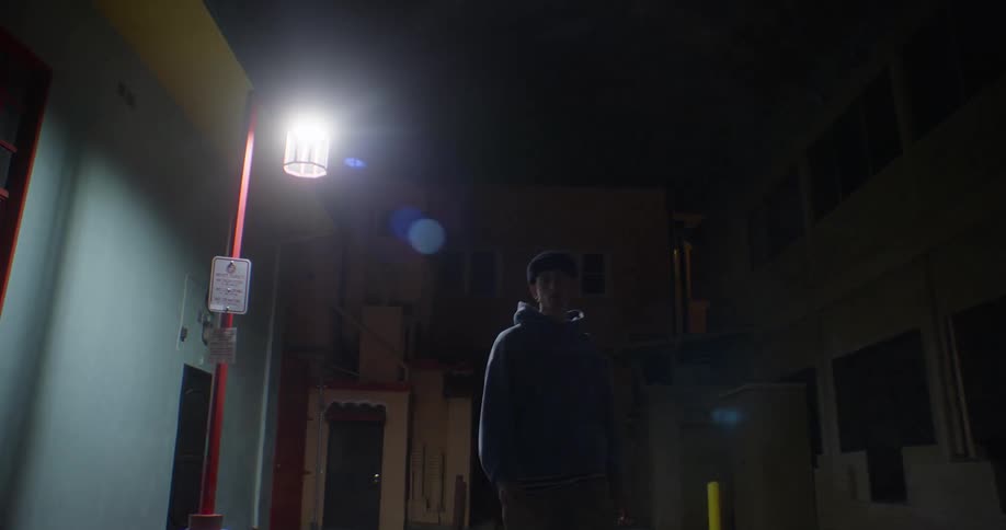 Man walks along the street between low rise buildings at night
