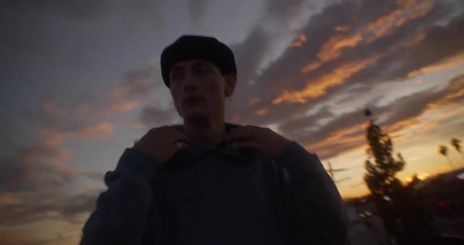 Young man walking outdoors in late afternoon and putting on his sweatshirt hood