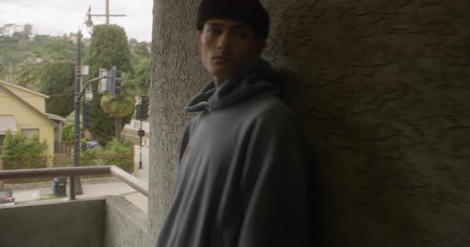 Man leans against a wall next to a balcony on an upper story of a residential building near an intersection during the daytime