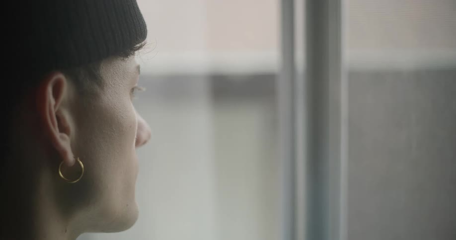 A man wearing a black beanie and a gold hoop earring gazes out of a window