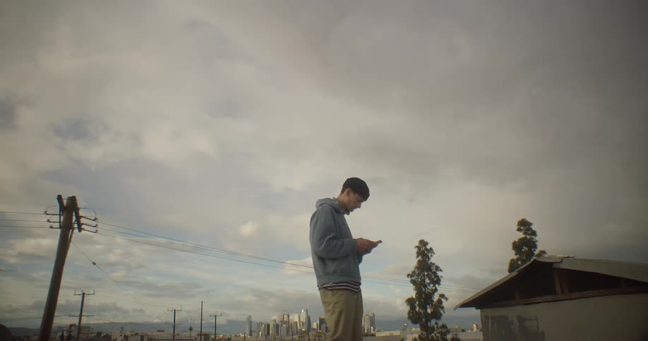 A young man stands outside in a residential neighborhood and texts on his smartphone