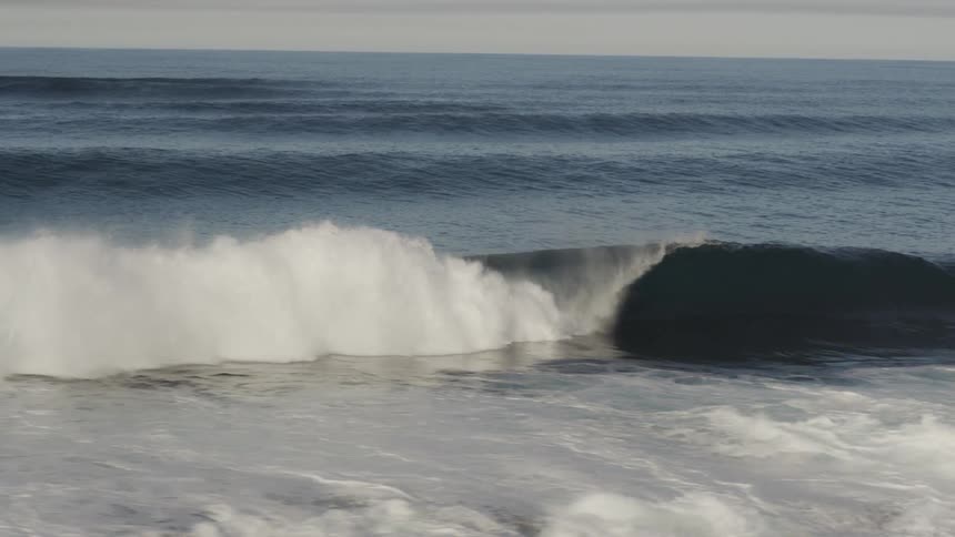 Aerial view of the ocean with a tubular wave breaking