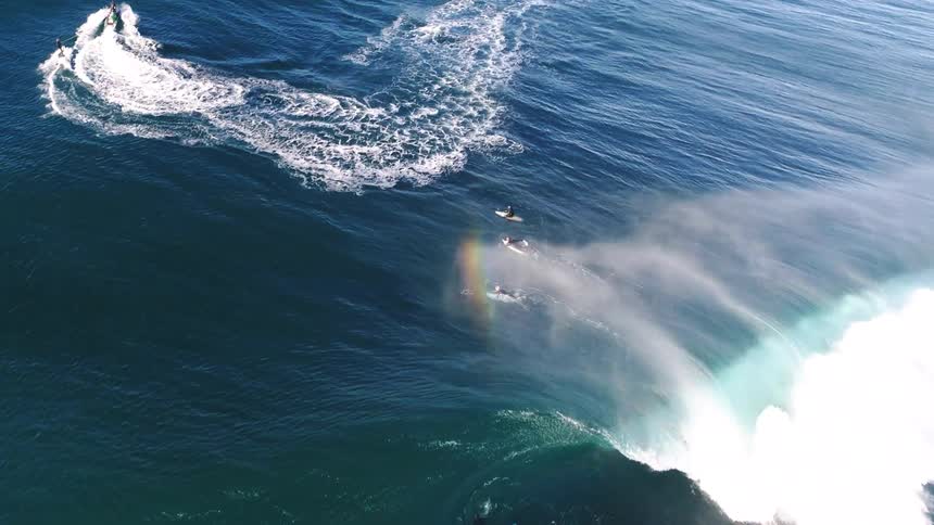 Surfers sit on their surfboards near a water skier as a wave passes beneath them
