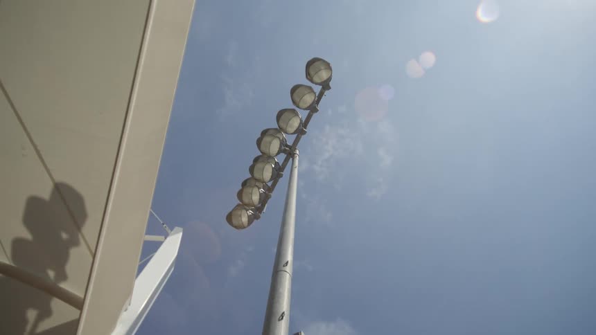 Lamppost with multiple bulbs towers over a structure on a sunny day