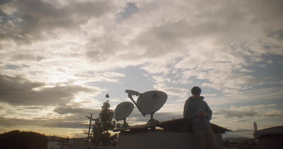 Young man uses his smartphone while leaning near two satellite dishes on a cloudy day