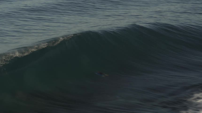 A gigantic wave crashes as a person on a surfboard rides it