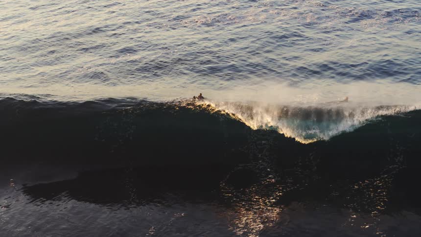 Wave swells and breaks under two surfers during the daytime