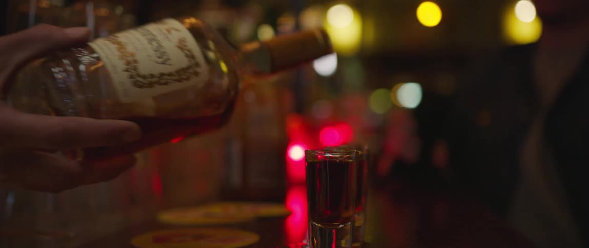 In a dimly lit bar with background bokeh hennessy cognac is poured from a bottle into a shot glass on the counter