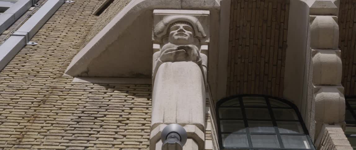 A stone figure is carved onto an exterior pillar of a brick building situated beside an arched window