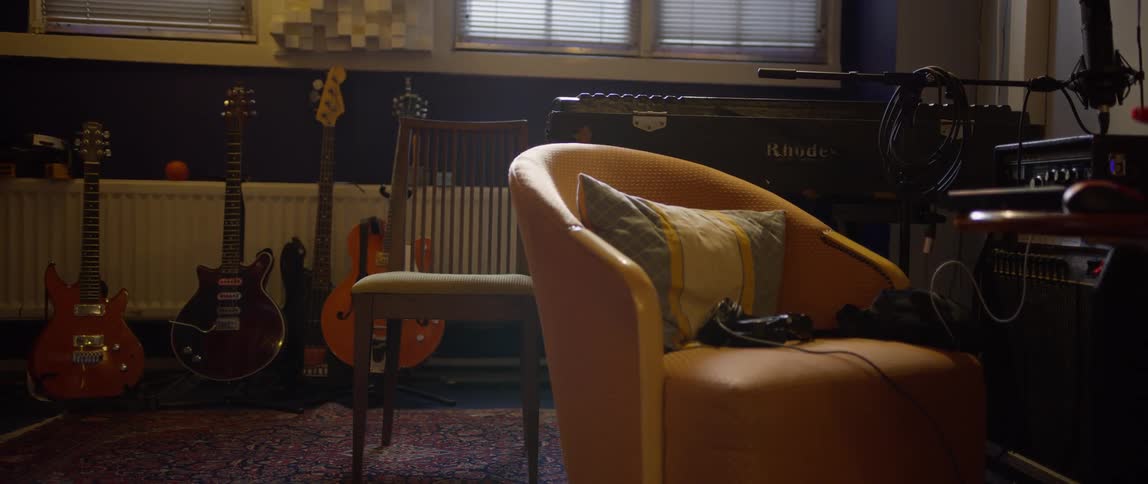 The interior of a music recording studio shows various guitars leaning against the wall an electric piano and an armchair in the foreground