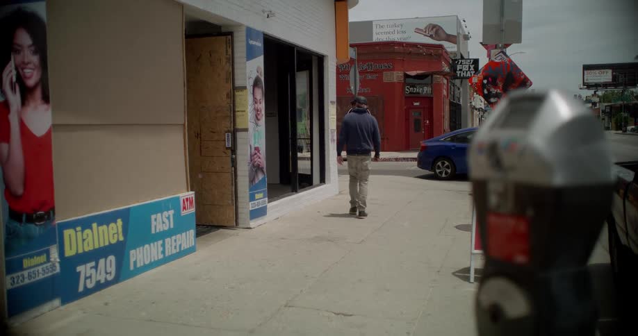 A man walks down a city sidewalk past various storefronts with a parking meter visible in the foreground