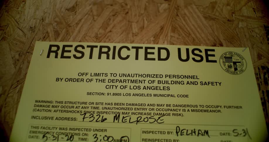 A closeup shows a yellow restricted use notice from the city of los angeles department of building and safety posted on a wooden board
