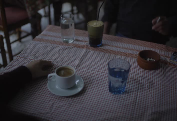 Two people sitting at a table with cup of coffee water and cigarette