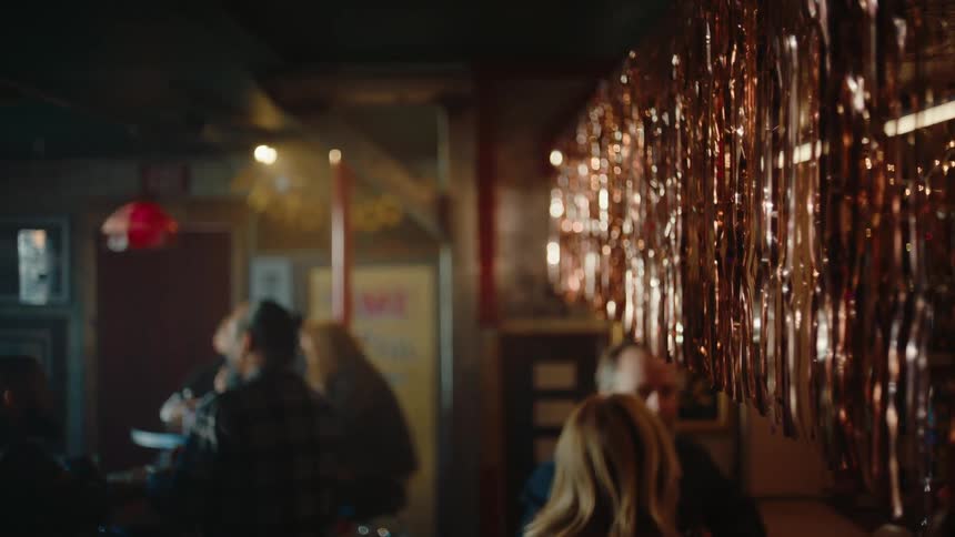 Shiny metallic streamers hang in the foreground partially obscuring the blurry view of patrons seated inside a dimly lit bar