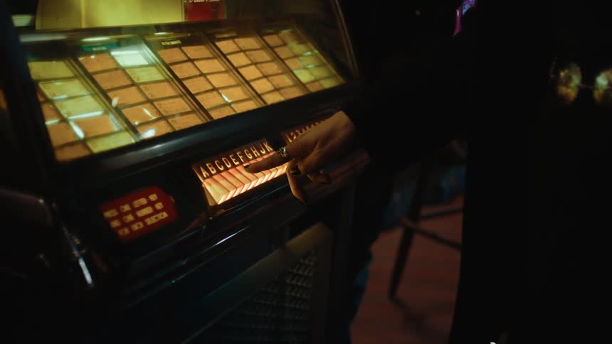 A woman wearing a dark dress with a gold colored belt chooses an option on an old jukebox