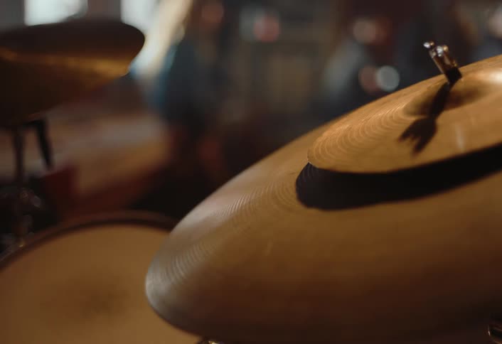 A brass drum cymbal vibrating and being hit by a drumstick in a dimly lit space