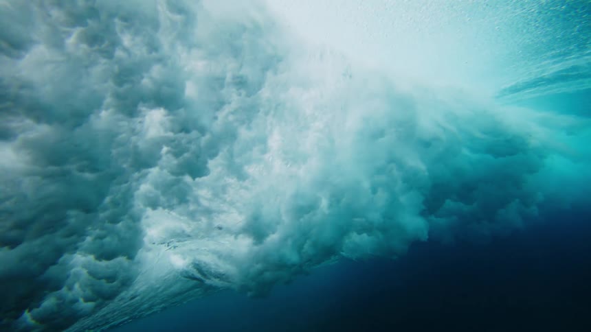 Rolling wave churns the water near the seafloor while people sit on surfboards above