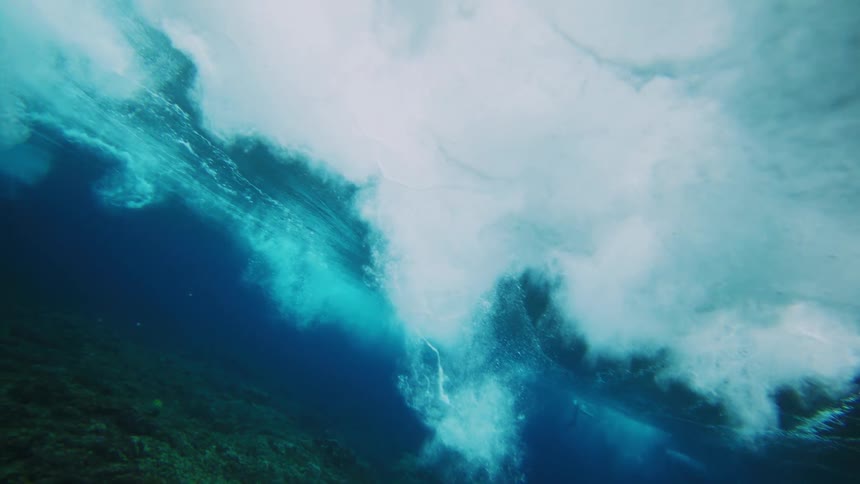 Underwater view of the ocean with corals and a foamy wave passing by