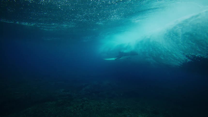 Submerged view in the ocean with a wave passing by and in the background a surfer with a surfboard