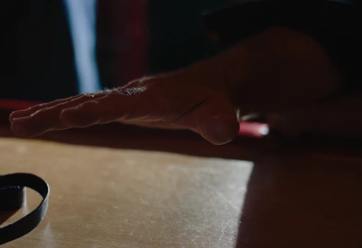 In a dimly lit bar a closeup shows an elderly mans hand spreading open across the wooden counter gesturing as if to show something near a drink