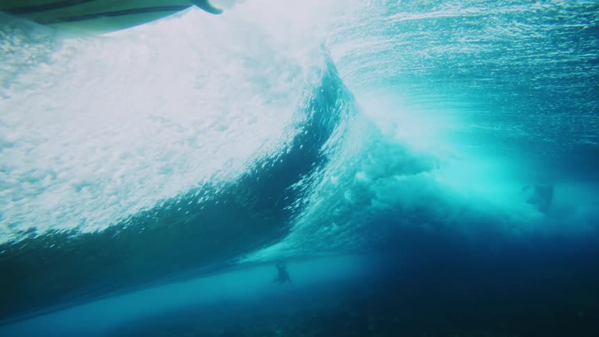 A wave rolls overhead near the ocean floor and the back of a surfboard shows through