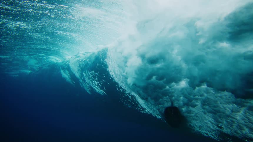 A surfboard riding a wave passes by above from underwater