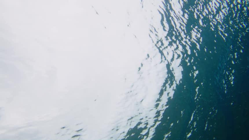 An underwater view looks up towards the shimmering surface as bubbles rise through the blue water