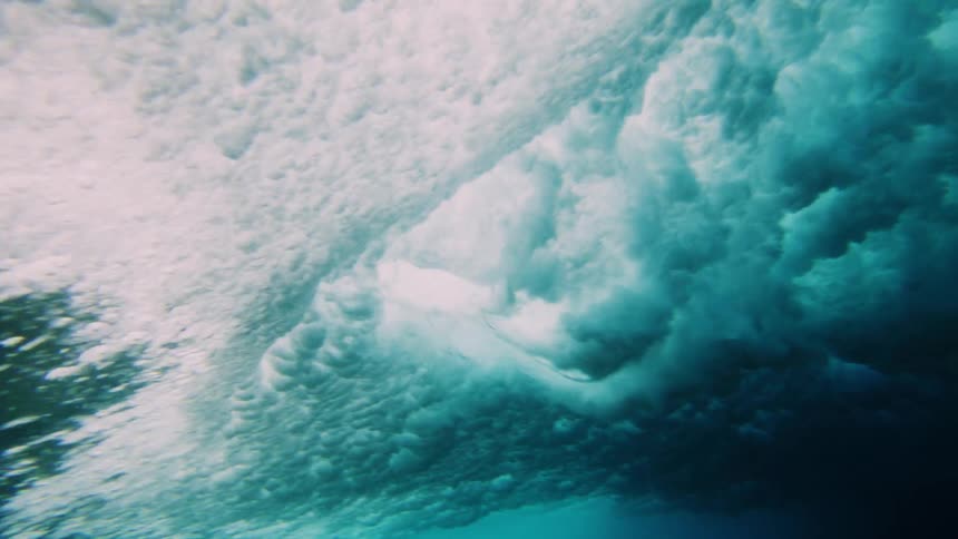 Underwater view and a wave passing by with two surfers