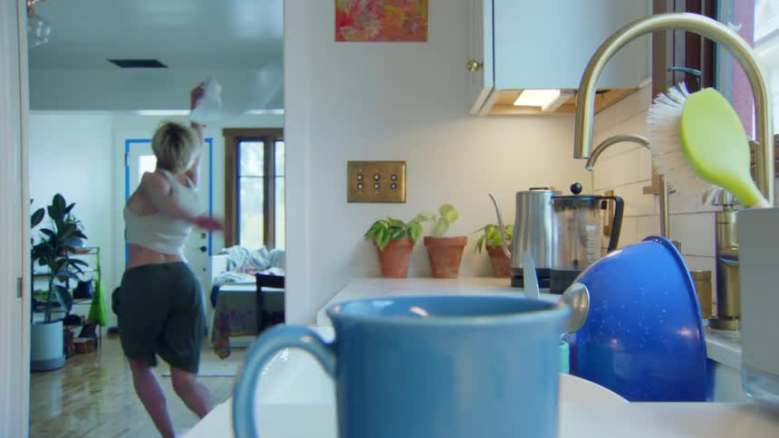 A woman washing dishes stops and runs to the living room dancing
